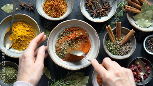 Overhead video of neutral hands meticulously arranging vibrant spices, herbs, and red berries on a dark slate with ceramic bowls. Macro close-ups under soft light, natural ingredients for healthy