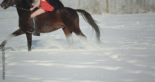 Woman riding galloping brown horse in winter snow