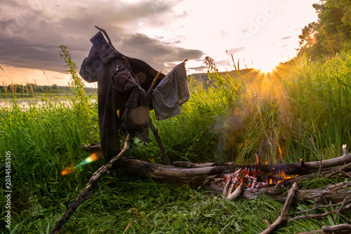 Fotografie Clothes drying on makeshift rack over campfire on riverbank with dark rain cloud