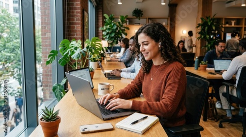 Young woman working on a laptop in a modern co-working space with plants.