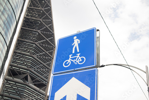 Low-angle view of a blue pedestrian and bicycle traffic sign in front of modern skyscrapers in an urban business district