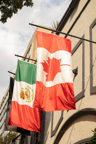 Canadian and Mexican national flags hanging on a building facade in an urban environment during daylight