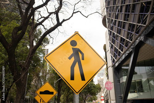 Yellow pedestrian crossing traffic sign in a modern urban environment surrounded by trees and contemporary office buildings
