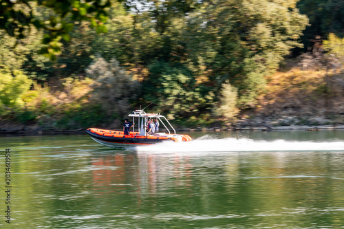 Obraz na plátně Red rigid inflatable rescue boat speeding down a green river leaving a white wak
