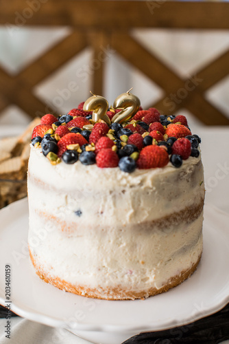 tall berry birthday homemade cake with candles 32 and white icing on a plate