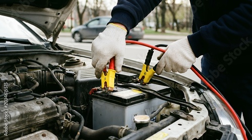 Close up shot of a person wearing white gloves attaching jumper cables to a car battery under the hood car engine mechanic automotive repair vehicle troubleshooting assistance