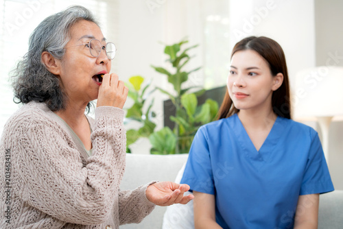 Asian senior woman eating medicine pill with caregiver support, elderly patient taking prescription drug at home, homecare service, doctor supporting elderly patient for disease treatment.