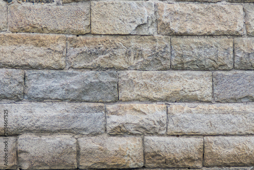 Close up view of weathered vertical stone masonry wall showing horizontal rows of large rectangular granite blocks
