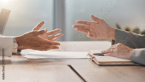 Two business people discuss documents and ideas across a wooden office desk with hands extended