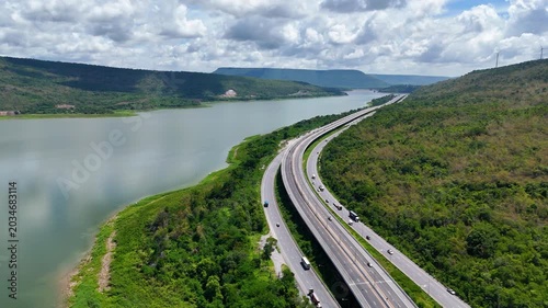 Aerial view of highway running along river and green hills. Transportation, infrastructure, travel and logistics concept