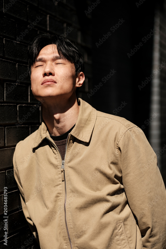 Fototapeta premium Young asian man closing eyes enjoying sunlight