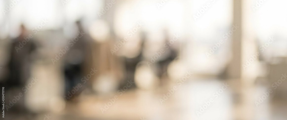Obraz premium A blurred office environment featuring people engaged in various activities, illustrating a busy and dynamic workspace filled with natural light.