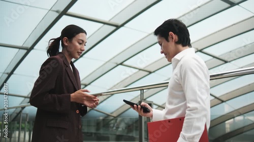 Young Asian smart businesspeople exchange digital contact information with NFC QR code, wireless mobile phone app technology, contactless startup collaboration at outdoor workplace, modern lifestyle.