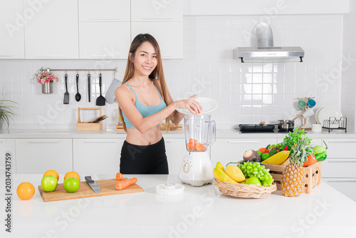 Healthy asian woman using blender in kitchen with cheerful smile and active pose making fresh smoothie