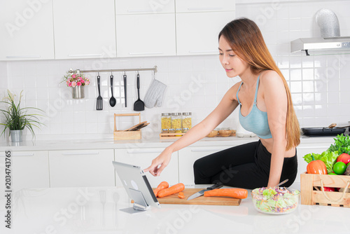 Asian woman following online cooking guide in modern kitchen
Description: Creative asian woman using tablet in kitchen with thoughtful expression and casual pose making healthy recipe