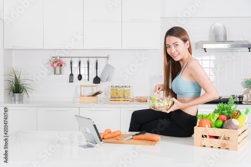 Fit asian woman eating salad in kitchen with happy smile and casual pose during healthy routine