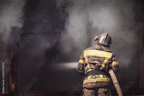 Bilde på lerret Firefighter spraying water to extinguish burning building in heavy smoke, emerge