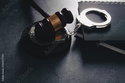 Judge gavel, handcuffs and notepad on black table background.