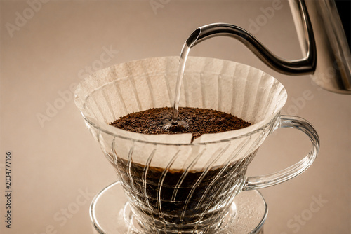 Hot water pouring from a stainless steel gooseneck kettle onto ground coffee in a paper filter.
