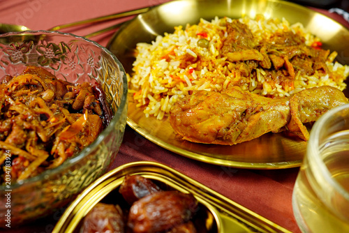 Flavorful chicken rice dish served with spicy curry, sweet dates and savory side snacks. Traditional halal cuisine for Ramadan iftar and festive Middle Eastern dining concepts.