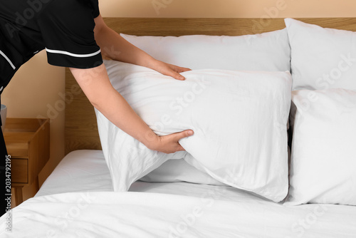 Young housemaid making bed ...