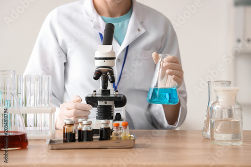 Female scientist with microscope and flask at table in laboratory, closeup