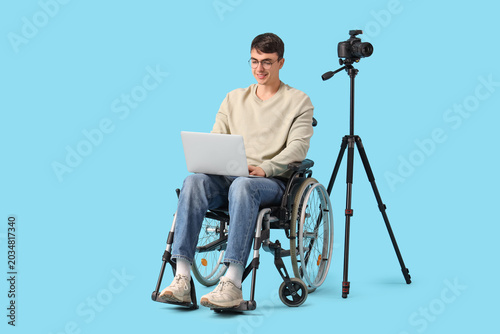 Male photographer in wheelchair with laptop and camera on blue background. Eq...