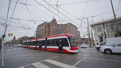 Urban public transit system showing a modern Toronto streetcar turning at city intersection with overhead power lines and historic brick buildings on overcast day