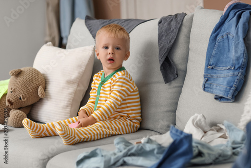 Bild auf Leinwand Naughty baby boy with toys and scattered clothes on sofa in messy room