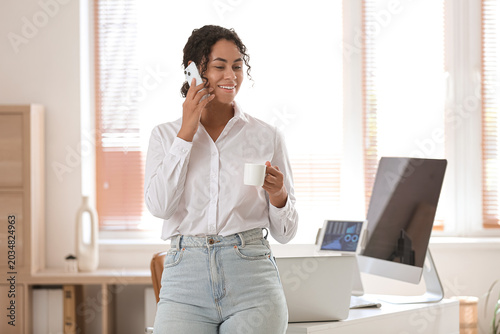 Young African-American QA engineer with cup of coffee talking by phone in office