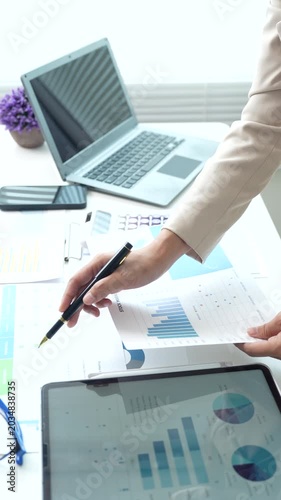 Business professional reviewing financial reports and performance charts at a modern office desk, analyzing data, planning strategy, and managing corporate documentation.