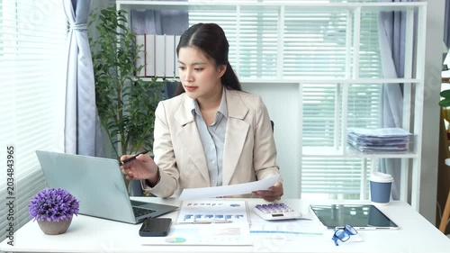 Young businesswoman reviewing financial documents and reports at a modern office desk, analyzing data and managing paperwork with focus and professionalism.