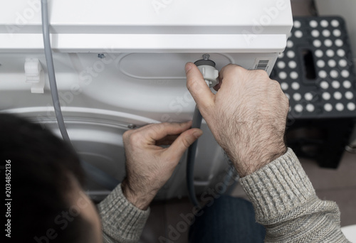 Plumber installing or removing washing machine transit shipping bolts. Man connecting water inlet and drain hose pipe. Plastic hole plugs, wrench tools. Home appliance installation concept.