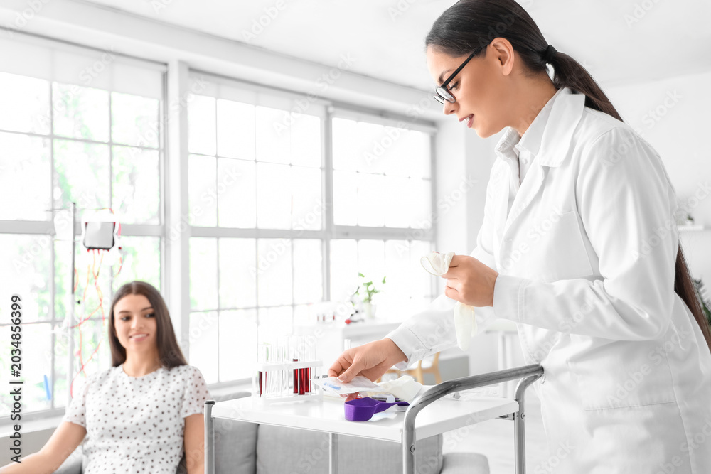 Fototapeta premium Female doctor preparing young donor for blood transfusion in clinic