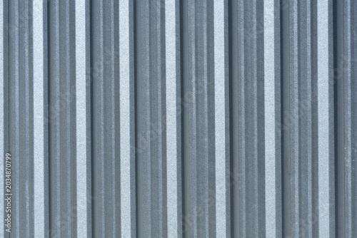 A full frame background texture of a grey corrugated zinc metal sheet with vertical ridges used for industrial fencing or roofing