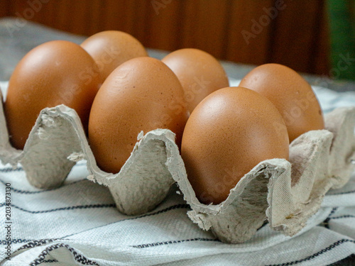 Fresh Brown Eggs in Grey Egg Carton on Striped Cloth