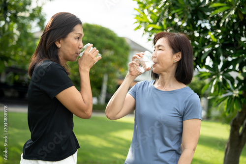 Two mature Asian women drinking water outdoors