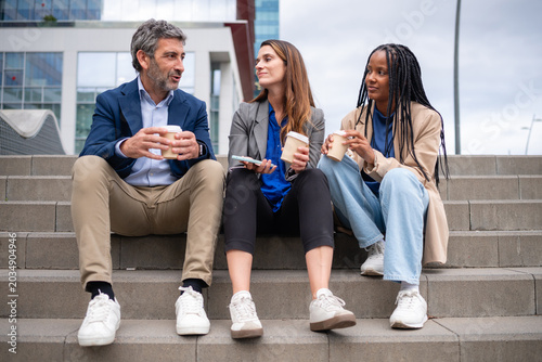 Diverse business people sharing coffee break on city stairs