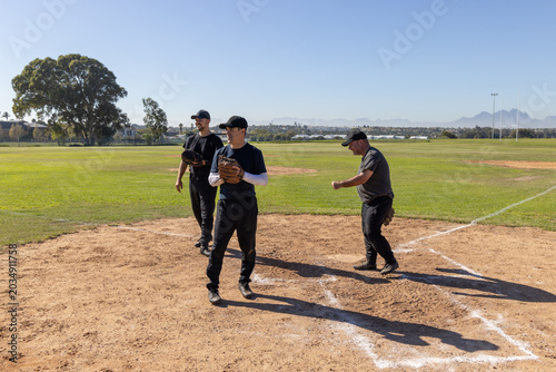 Photos Three male baseball players in black uniforms warming up on infield at home plat