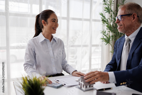 Real estate agent explaining housing loan details to a smiling client, discussing property ownership documents and home investment options in a modern office