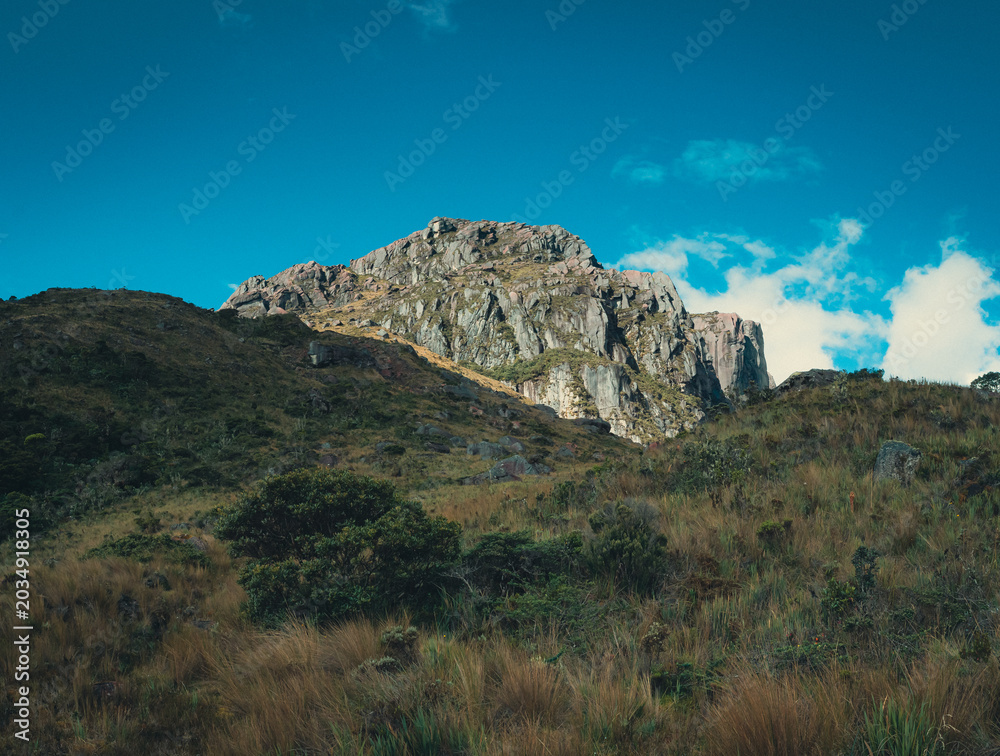 Fototapeta premium Rocky Andean mountain peak with highland páramo vegetation under blue sky in Ecuador