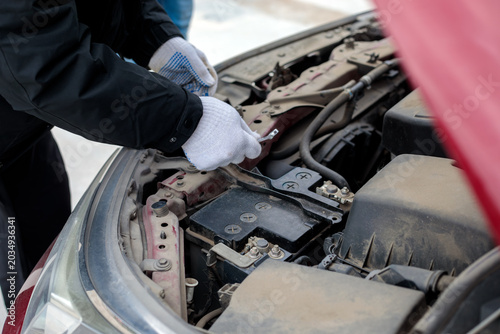 Tableau sur toile Hands in white gloves replacing or checking car battery in engine compartment under open hood