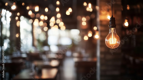 Vintage incandescent light bulb glowing in a blurred cozy cafe background with warm bokeh lights