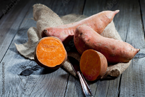 Row sweet potatoand knife on jute, wood