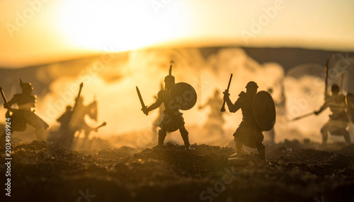 Silhouette of medieval warriors with swords and shields in battle scene at sunset