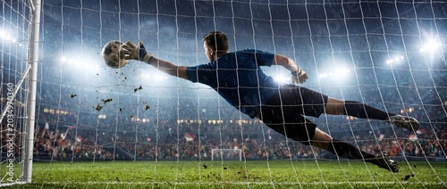 Soccer goalkeeper diving to catch ball at night stadium with crowd