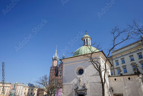St. Adalbert's Church in Krakow's Market Square. A 16th-century church. The tower of St. Mary's Church in the background. Church and tower stand in the sunlight in Krakow, Poland with a clear blue sky