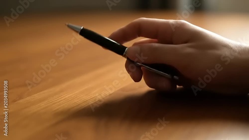 Hand Reaching for a Pen on a Wooden Table Surface.