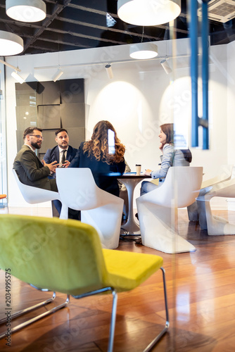 Business team collaborating in modern office lounge, discussing strategies during a corporate meeting, having a professional discussion