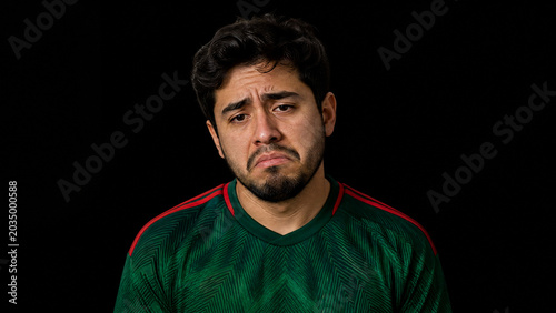 Displaying Hispanic man wearing green football jersey with red stripes in studio, sad expression